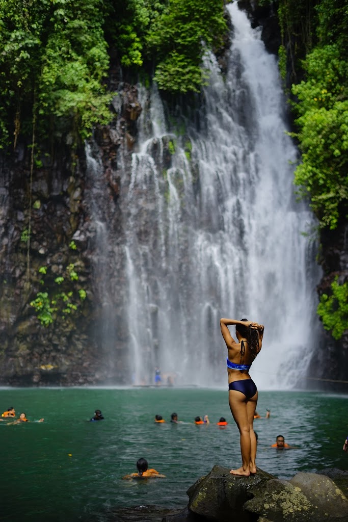 a lady in bikini standing in front of a waterfalls