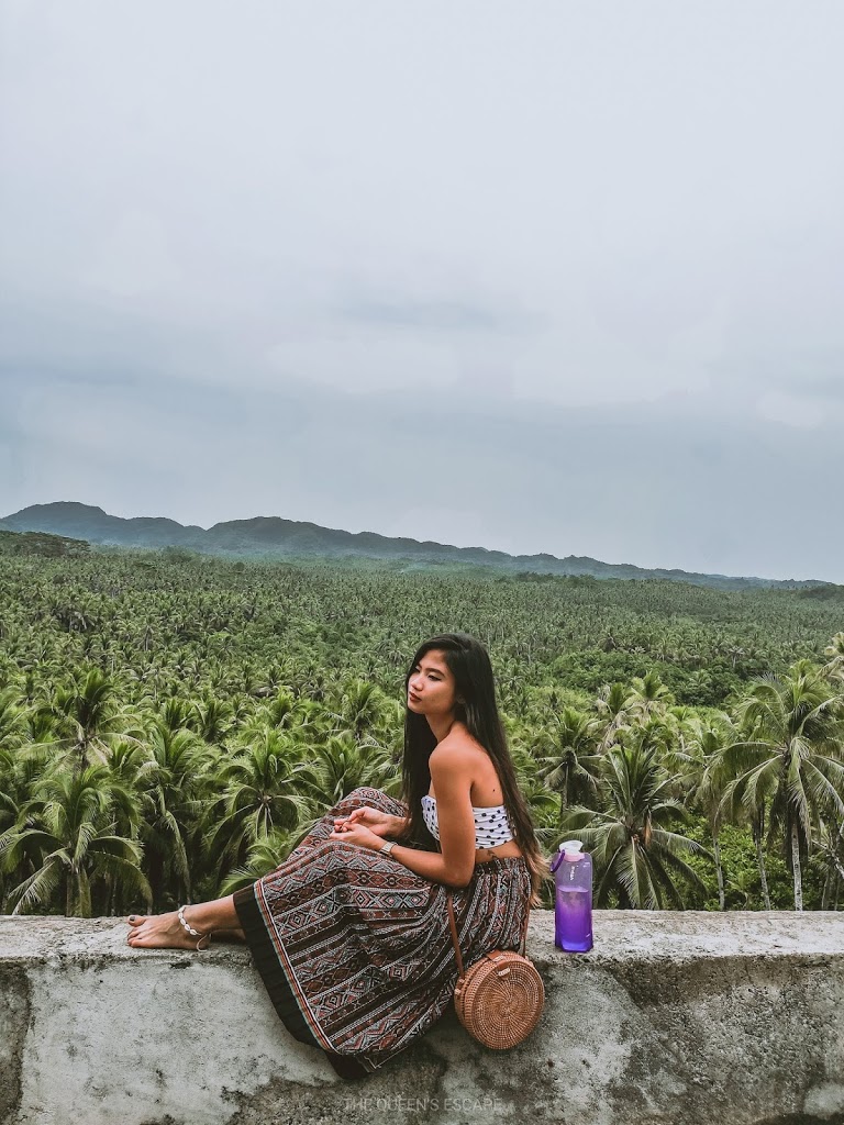 a girl sitting on a concrete bench overlooking the top of coconut trees