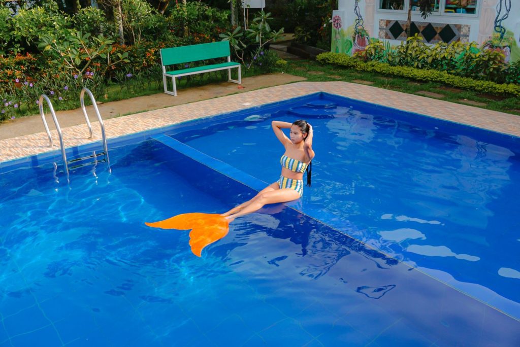 a lady in an orange mermaid fin seated at the pool